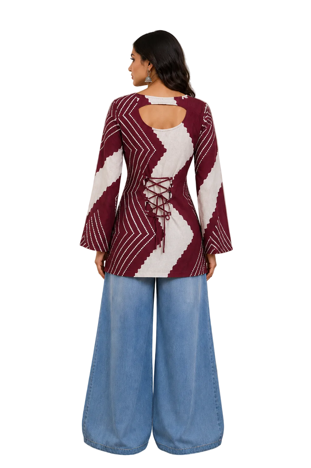 A woman stands with her back to the camera wearing a maroon and white patterned long-sleeve top with lace-up back detail, paired with wide-leg light blue jeans in a styled indoor room.