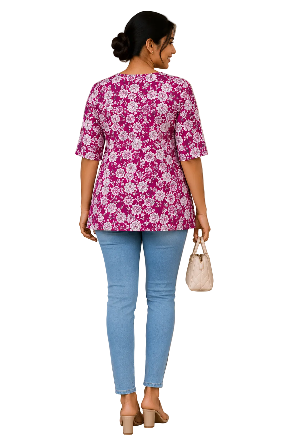 A woman viewed from behind wearing a pink and white floral print short-sleeve top, light blue jeans, and beige heels, holding a small cream handbag in an indoor setting.