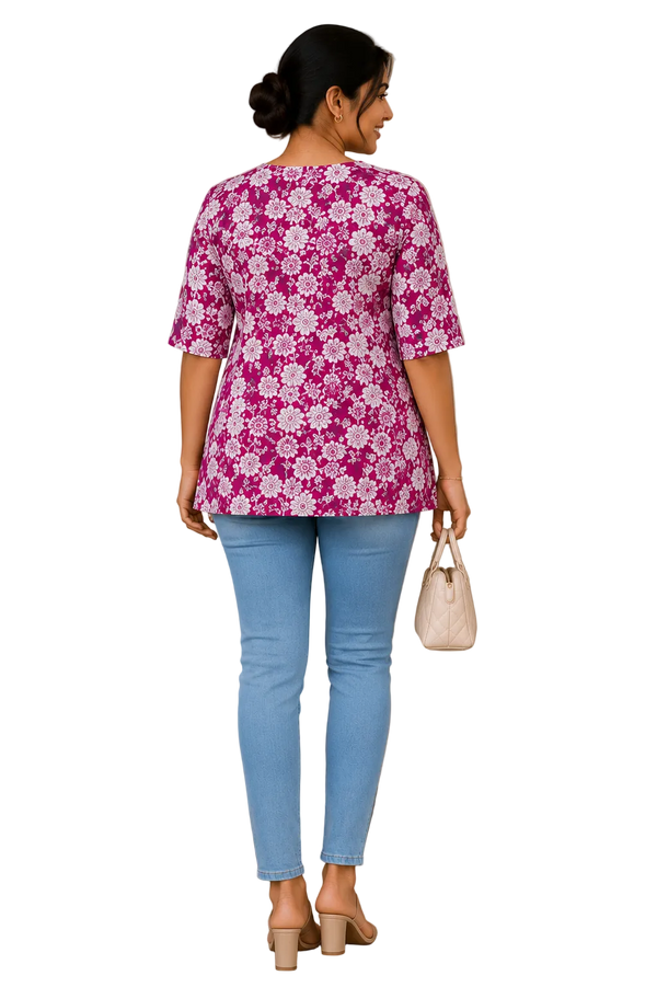 A woman viewed from behind wearing a pink and white floral print short-sleeve top, light blue jeans, and beige heels, holding a small cream handbag in an indoor setting.