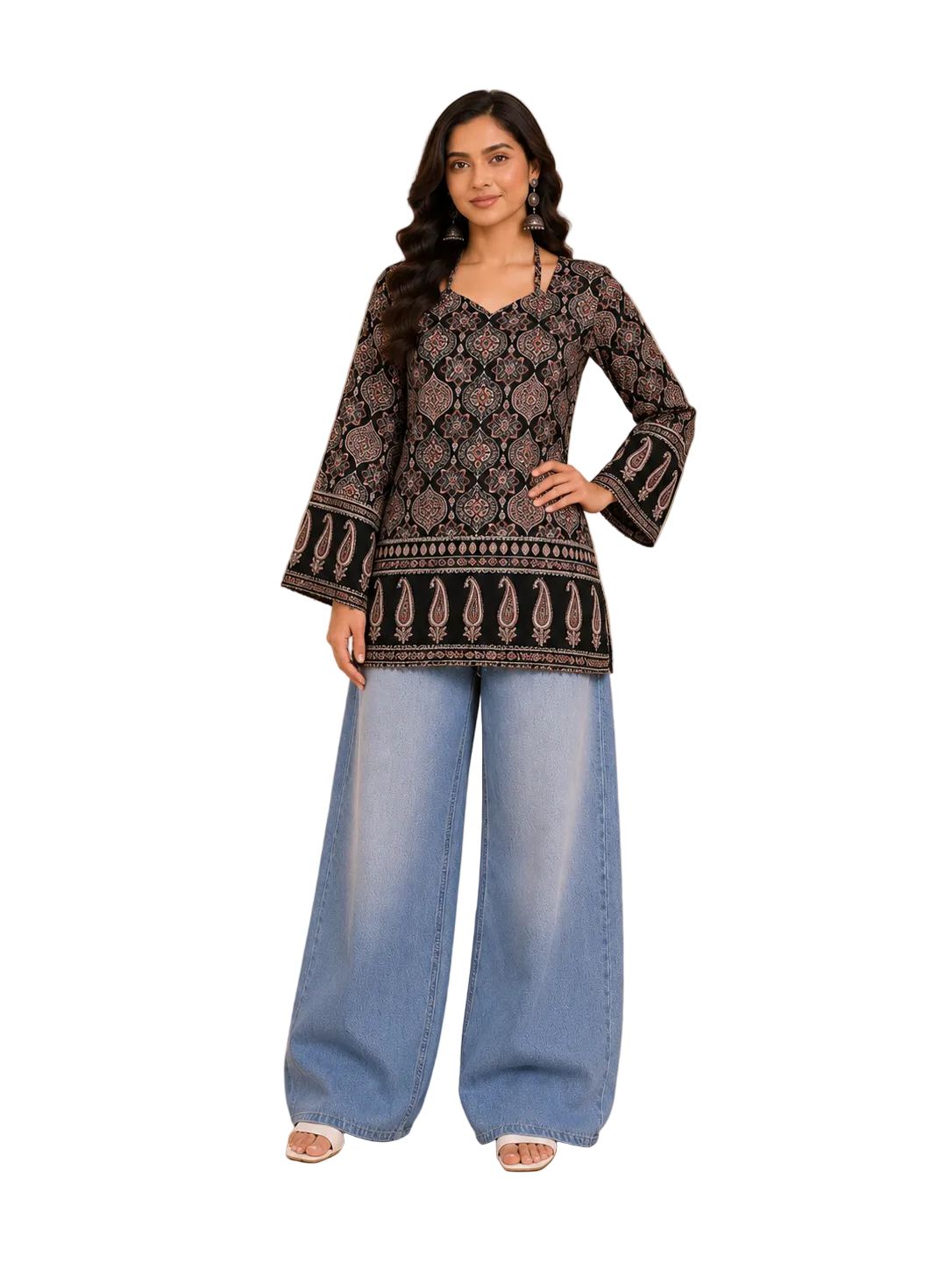 A woman modeling a black embroidered kurta with beige floral patterns and wide-leg light blue jeans, standing in a warm beige room with decorative shelves and a wooden bench.
